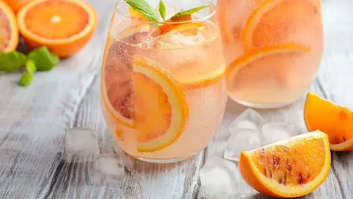 Refrescante agua de valencia con rodajas de naranja y menta, servida con hielo sobre una mesa de madera.