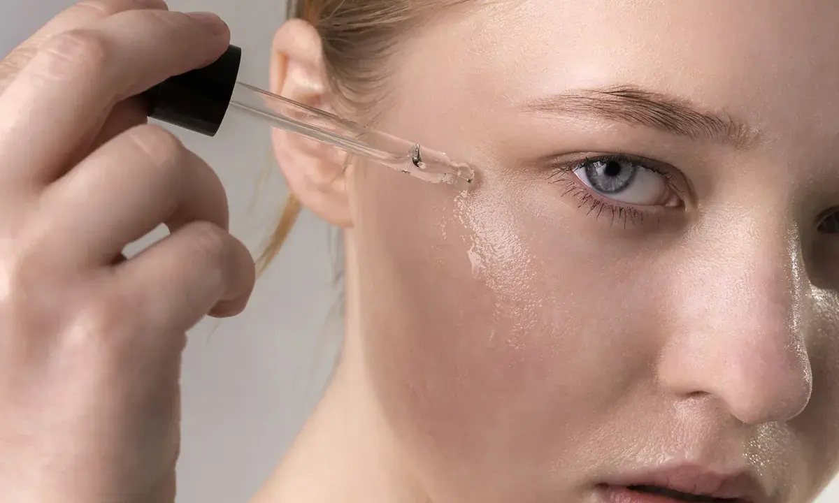 Una mano aplica suero con retinol en la mejilla de una mujer. El retinol para que sirve: rejuvenece la piel.