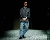Matthieu Blazy, diseñador de Bottega Veneta, sonríe en la pasarela con camisa gris y vaqueros.
