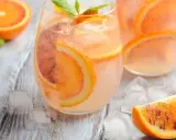 Refrescante agua de valencia con rodajas de naranja y menta, servida con hielo sobre una mesa de madera.