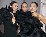 Tres modelos lucen peinados recogidos elegantes, perfectos para una fiesta, con vestidos negros voluminosos y detalles de volantes.