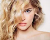 Mujer rubia con ondas, delineado de ojos y labios rosados. Un ejemplo de trucos de belleza para realzar la mirada.