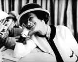 Coco Chanel, sonriendo con un sombrero y perlas, evoca la elegancia de donde es Chanel.