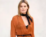 Camille Rowe luce un pañuelo negro y un vestido naranja con escote pronunciado.