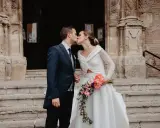 Novios besándose frente a una iglesia, ella lleva un ramo de flores. Un momento especial tras las lecturas de boda religiosa.