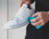 Manos limpiando zapatillas blancas de tela con un paño azul.