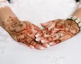 Manos de novia con intrincados diseños de henna, anillos y pulsera brillante, listas para la boda.