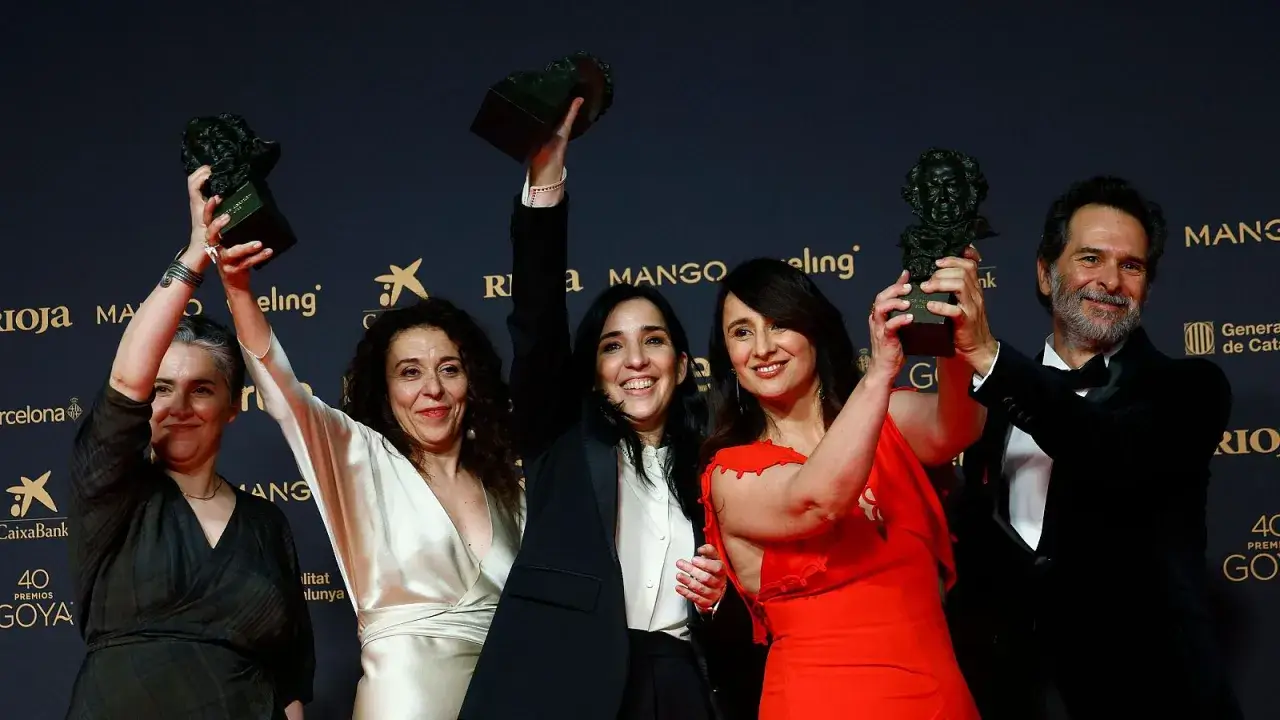 Ganadores celebran sus premios Goya 2026. Cinco personas sonríen alzando estatuillas doradas sobre un fondo oscuro con logos de patrocinadores.