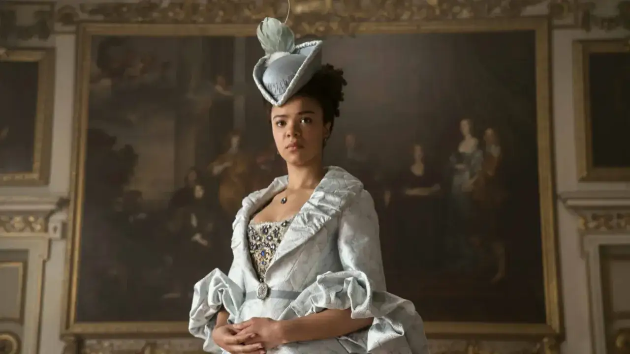 Joven reina Carlota, con un elegante vestido azul claro y un sombrero emplumado, posa ante un retrato familiar.