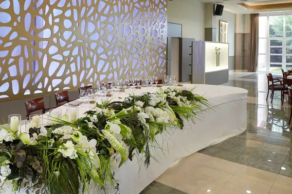 Elegante mesa presidencial boda con arreglos florales blancos y verdes, velas y copas.