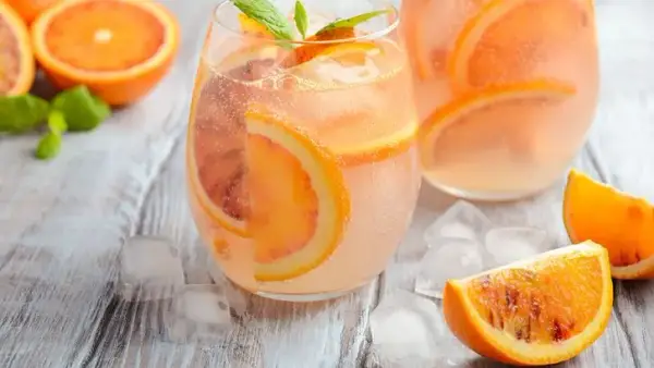Refrescante agua de valencia con rodajas de naranja y menta, servida con hielo sobre una mesa de madera.