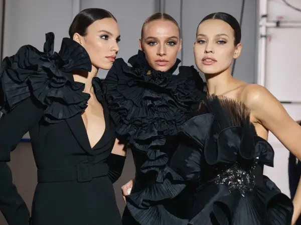 Tres modelos lucen peinados recogidos elegantes, perfectos para una fiesta, con vestidos negros voluminosos y detalles de volantes.