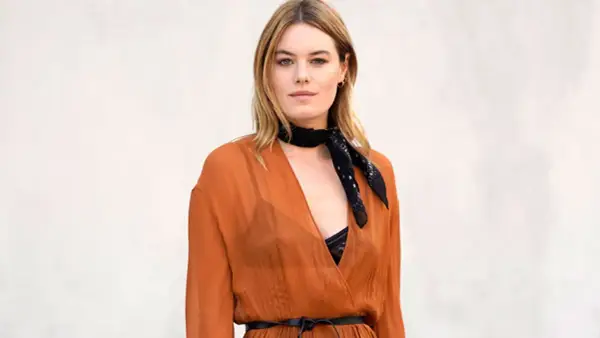 Camille Rowe luce un pañuelo negro y un vestido naranja con escote pronunciado.