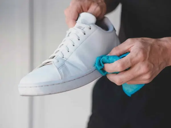 Manos limpiando zapatillas blancas de tela con un paño azul.