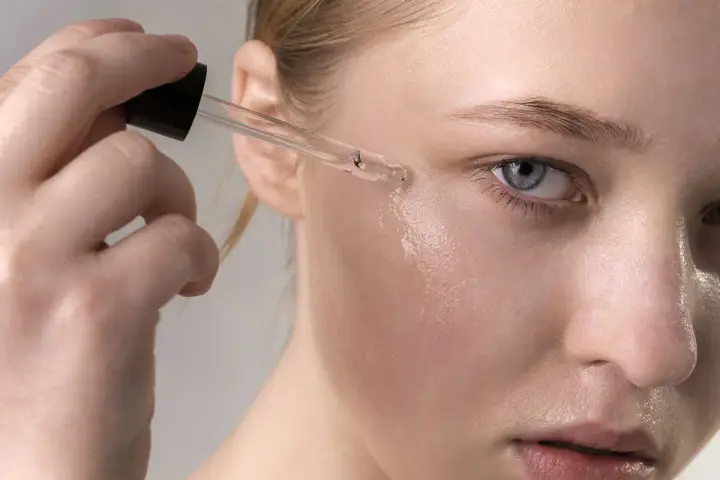 Una mano aplica suero con retinol en la mejilla de una mujer. El retinol para que sirve: rejuvenece la piel.