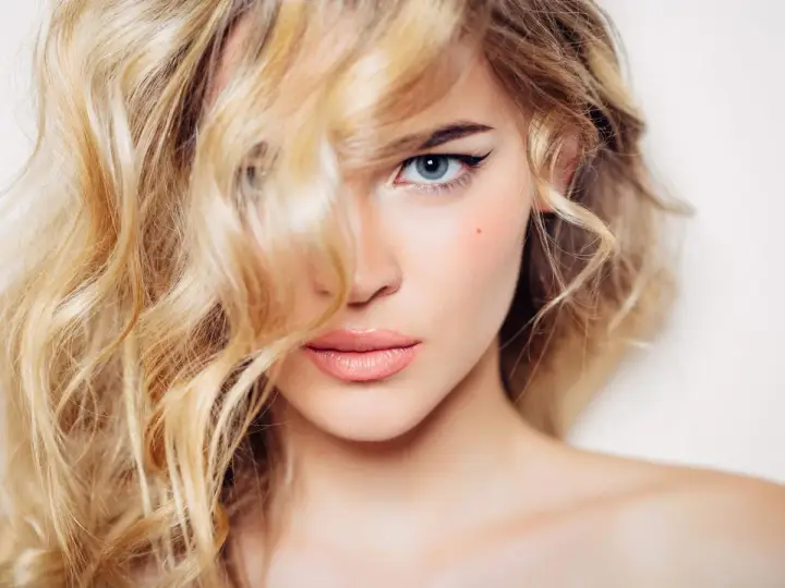 Mujer rubia con ondas, delineado de ojos y labios rosados. Un ejemplo de trucos de belleza para realzar la mirada.