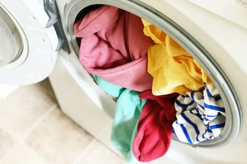 Carga de lavadora con ropa de colores variados, incluyendo rosa, amarillo, turquesa y rayas azules. ¡A ver si se puede lavar ropa blanca con ropa de color sin problemas!