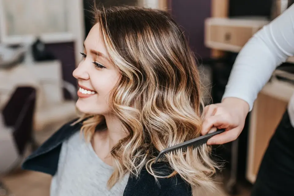 Mujer sonríe mientras le peinan su cabello con mechas balayage, luciendo un estilo moderno y natural.
